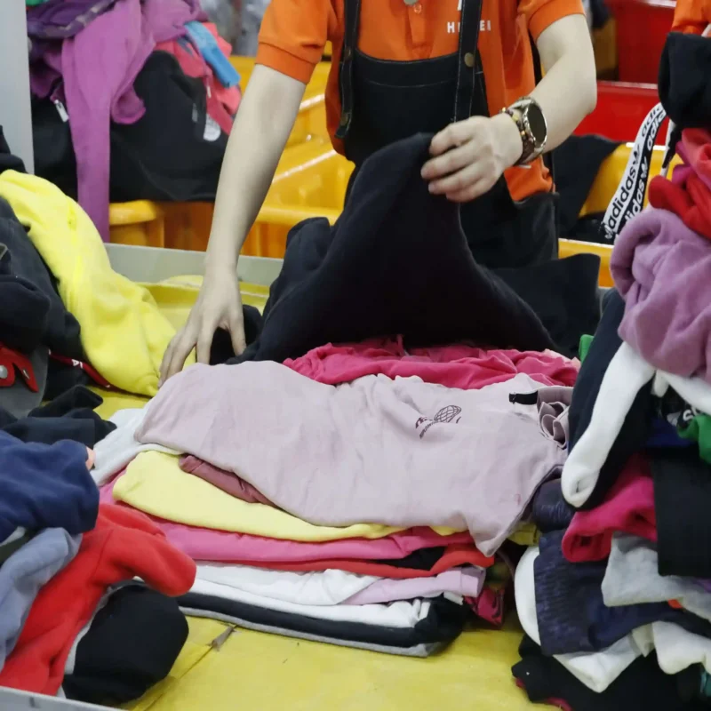 Trabajador separando manualmente prendas de ropa usada en una mesa de clasificación